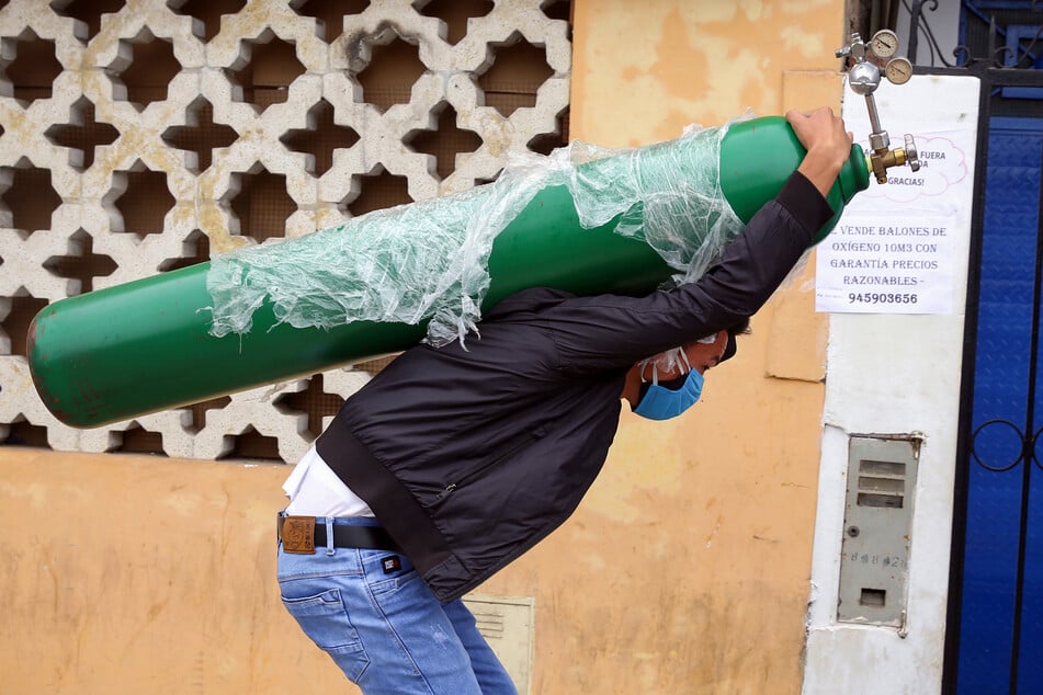 Ein Mann mit doppeltem Mundschutz trägt eine nachgefüllte Sauerstoffflasche auf dem Rücken. (Archivbild)