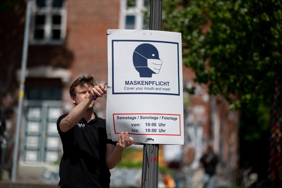 Ein Mitarbeiter hängt im Park Fiction in Hamburg ein Hinweisschild zur Maskenpflicht ab.