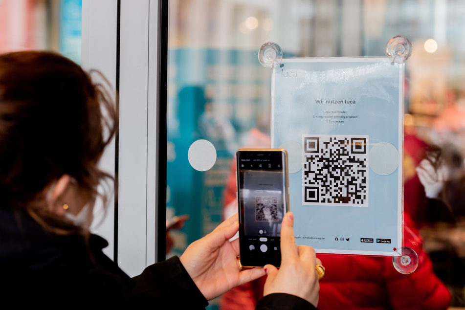 Eine Frau scannt am Eingang eines Bekleidungsgeschäftes einen QR-Code zum Download der Luca-App.