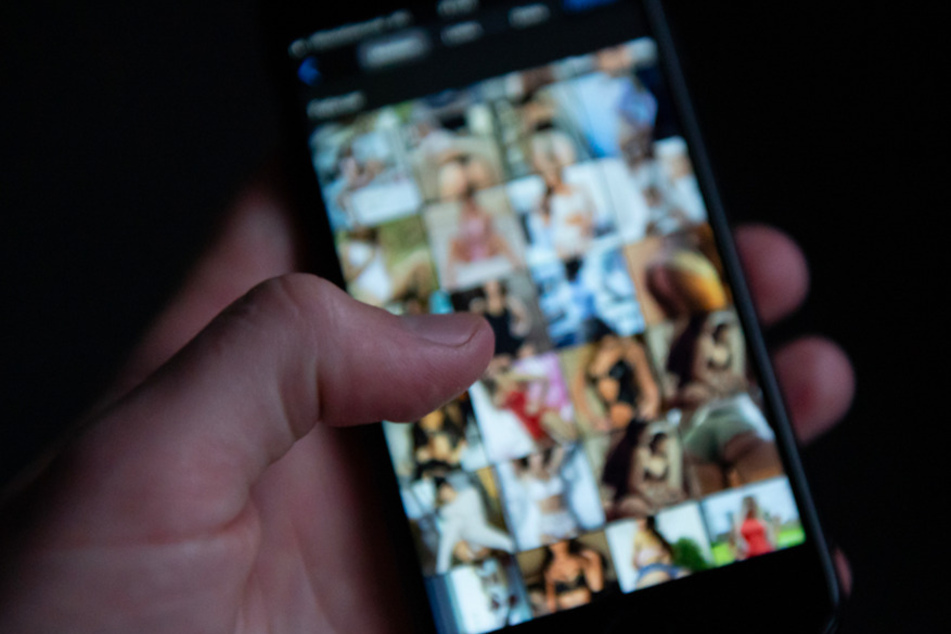 Ein Mann schaut sich auf einem Smartphone pornografische Bilder an. Ein Verdächtiger aus dem Kreis Erding, soll ein Mädchen zu Nacktfotos gedrängt haben. (Symbolbild)
