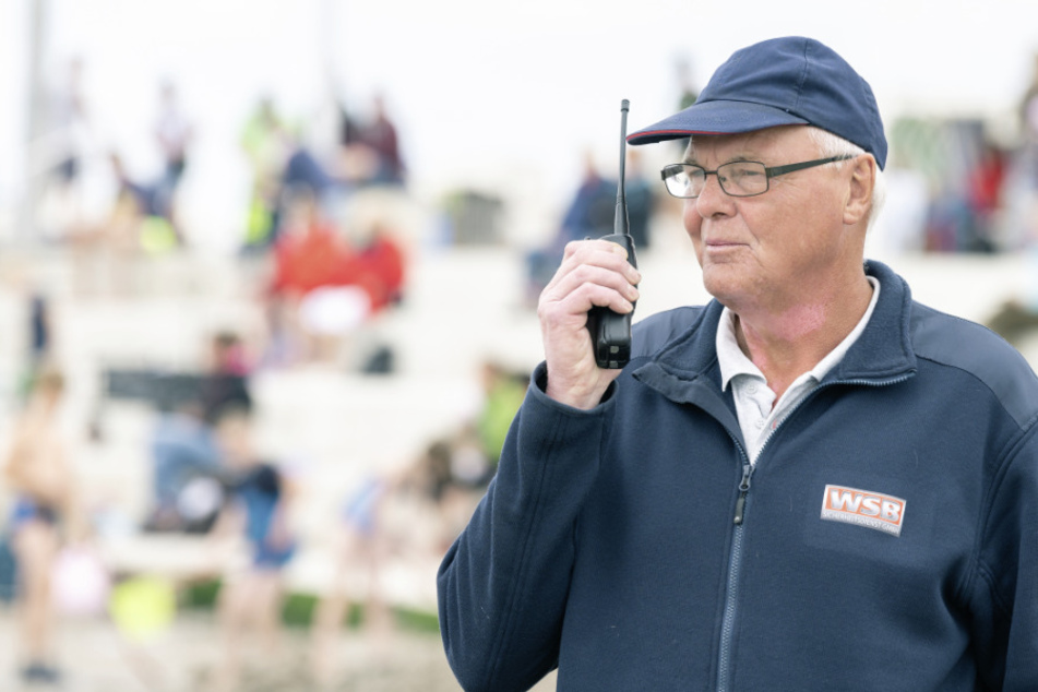Georg Ulrichs, Sicherheitskraft der WSB-Sicherheitsdienst GmbH, steht während seines Kontrollrundgangs am Badestrand von Norddeich und spricht über ein Funkgerät mit einem Kollegen.