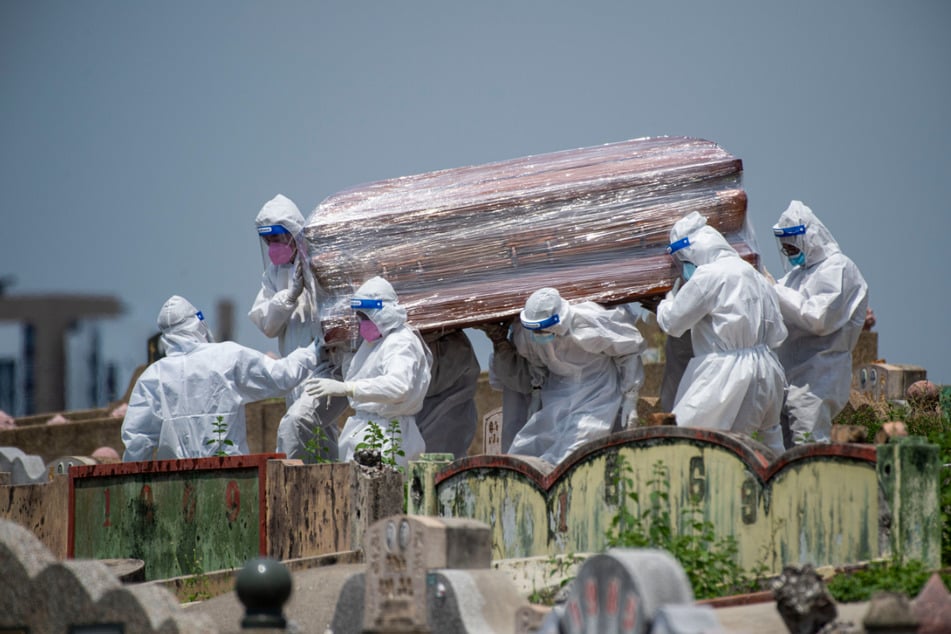 Malaysia, Selangor: Menschen in Schutzanzügen tragen den Sarg eines Corona-Opfers auf einen Friedhof.