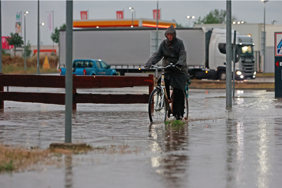 Eine Frau fährt nach dem Unwetter mit ihrem Fahrrad über eine überflutete Straße in einem Gewerbegebiet bei Blankenburg.
