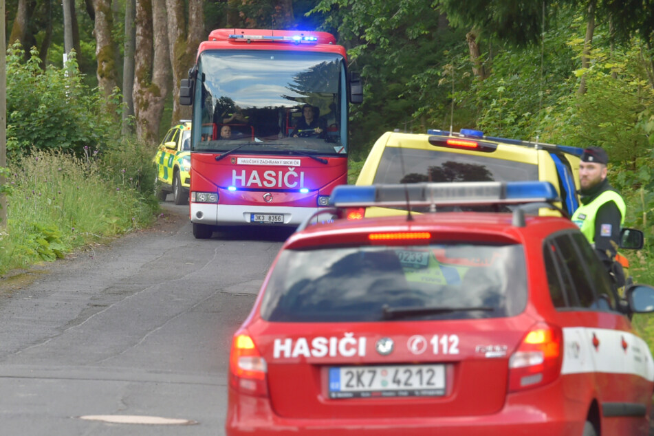 Ein Bus der Feuerwehr sowie Rettungskräfte stehen in der Nähe eines Zugunglücks an einer Straße.