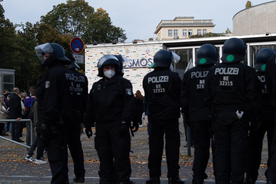 Teilnehmer der Demonstration gegen die Corona-Auflagen stehen vor dem Kosmos. Polizisten beobachten das Geschehen.