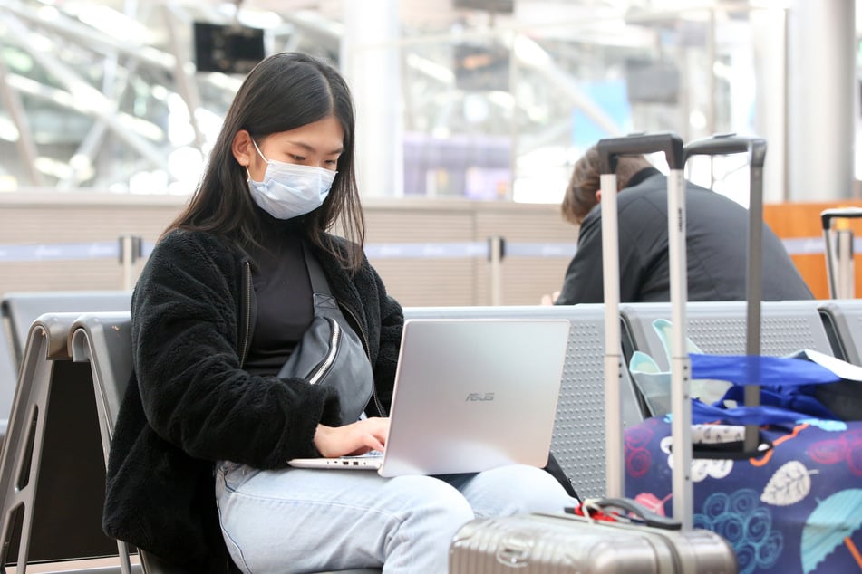 Ein junge Frau aus Indonesien sitzt mit einem Mundschutz in einer Abfertigungshalle im Flughafen Hamburg.