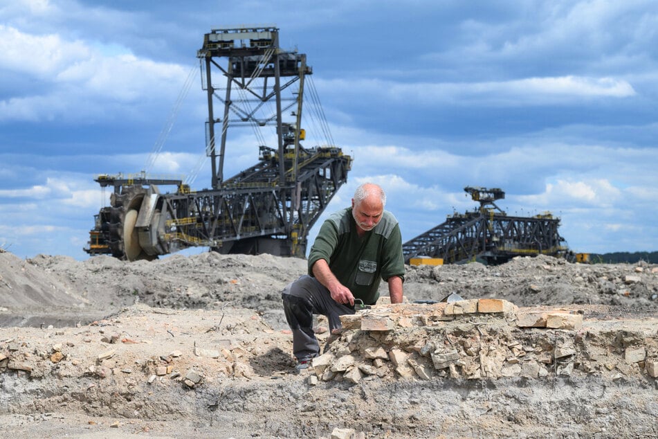 Grabungsleiter Jos Janssen auf dem Grabungsfeld im Tagebaugebiet von Nochten, im Hintergrund ist ein Vorschnittbagger der Lausitz Energie Bergbau AG (LEAG) zu sehen.