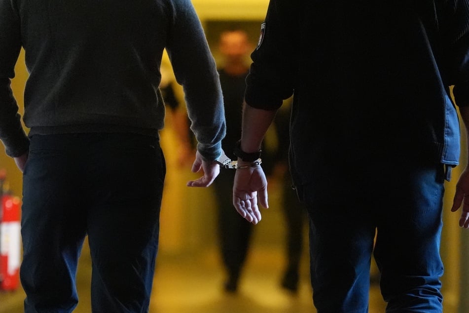 Die Angeklagten (l. und h. M.) wurden in Handschellen von Justizbeamten über einen Flur zum Sitzungssaal im Strafjustizgebäude gebracht.