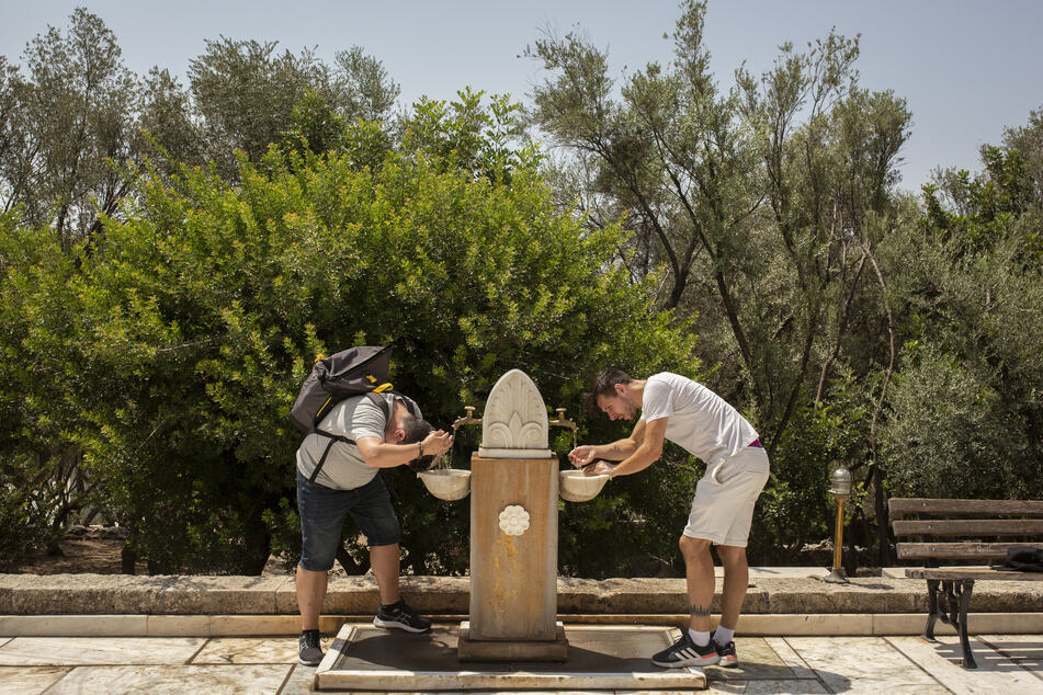 Touristen erfrischen sich während ihres Besuchs auf der Akropolis im Zentrum Athens an einem öffentlichen Trinkbrunnen.