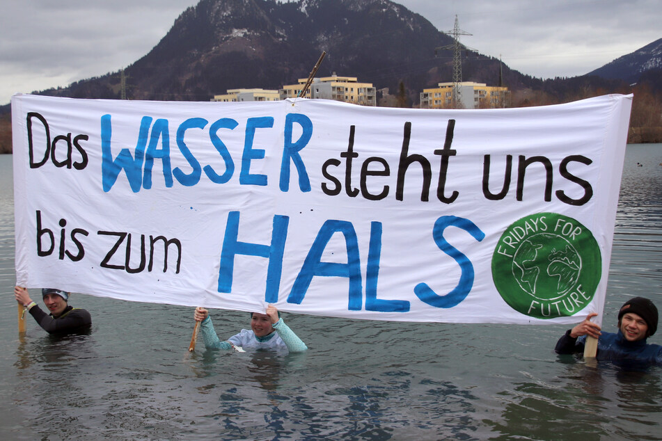 Klimaaktivisten stehen unter einem Transparent mit der Aufschrift "Das Wasser steht uns bis zum Hals" im Sonthofer See.