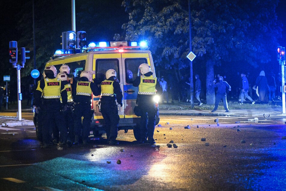 Demonstranten werfen während eines Protestes Steine auf Polizisten, die auf einer Straße hinter ihrem Fahrzeug stehen.