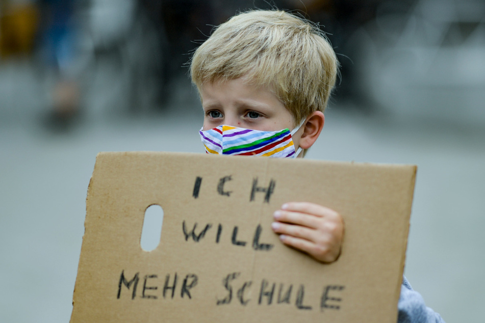 Ein Junge trägt einen bunt gestreiften Mund-Nasenschutz, während er ein Stück Pappkarton mit der Aufschrift "Ich will mehr Schule" auf dem Gänsemarkt in Hamburg vor sich hält.