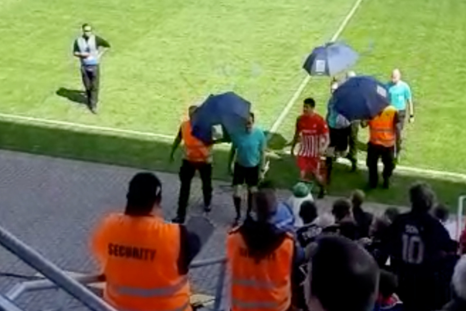 Amüsierter Applaus, als die Schiedsrichter nach der ersten Halbzeit von der Security mit Regenschirmen begleitet wurden.