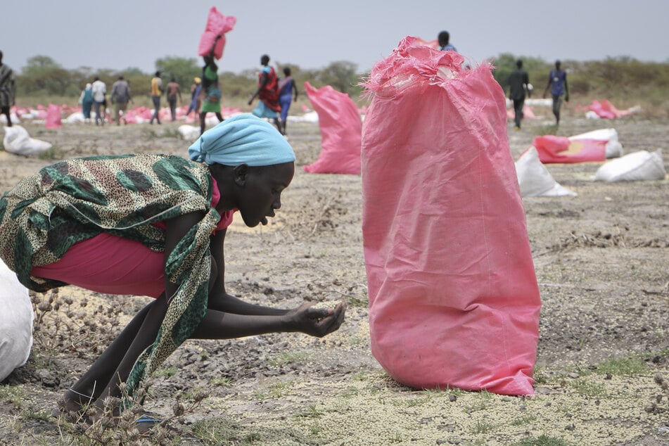 Südsudan, Kandak: Eine Frau sammelt Hirse vom Boden auf, die in Säcken vom Welternährungsprogramm (WFP) der Vereinten Nationen über der Stadt abgeworfen wurden.