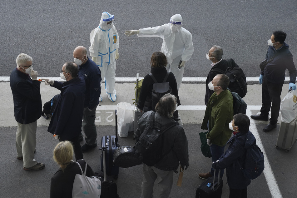 Arbeiter in Schutzkleidung sprechen mit Mitgliedern eines Teams der Weltgesundheitsorganisation (WHO) am Flughafen in Wuhan.