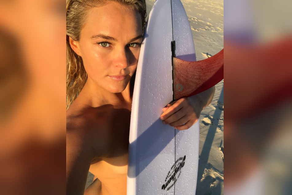 Felicity Palmateer (28) fotografiert sich nackt mit Surfbrett am Strand.