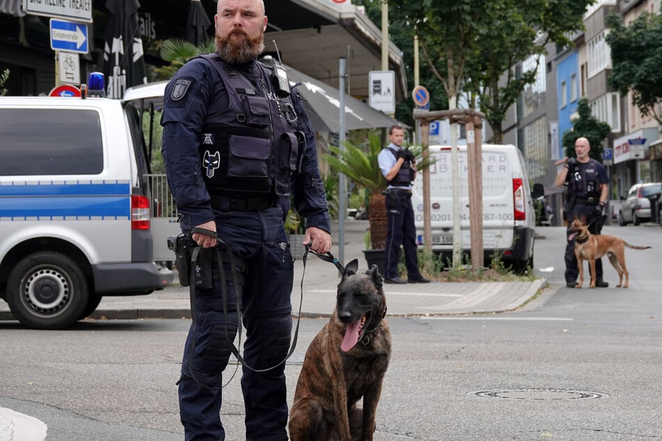 Ein Diensthundeführer steht in Essen mit seinem Polizeihund auf der Straße vor einer Bar. (Foto: Johannes Neudecker/dpa)
