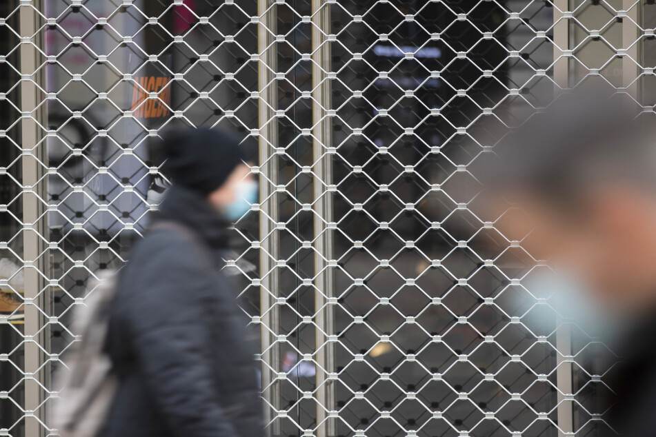 Menschen mit Mundschutz gehe an einem geschlossenen Geschäft in der Stuttgarter Königsstraße vorbei.