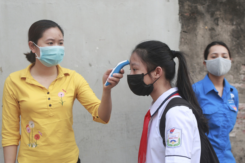 Bei einer Schülerin wird mithilfe eines Thermometers ein mögliches Fieber gemessen, bevor sie in die Dinh-Cong-Mittelschule in der vietnamesischen Hauptstadt Hanoi geht. (Archivbild)
