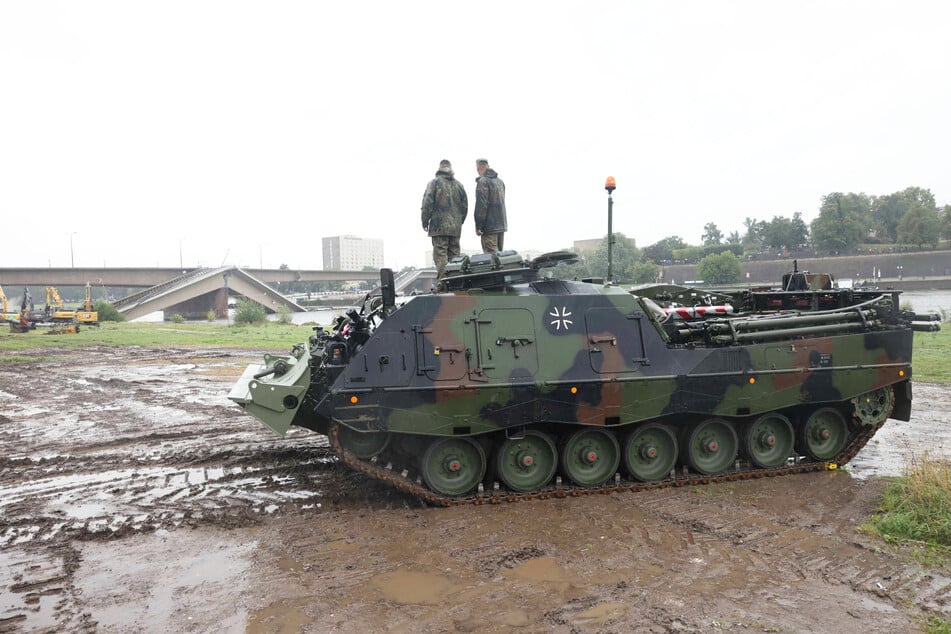 Zwei Bundeswehr-Männer stehen auf einem der Bergepanzer nahe der Carolabrücke.