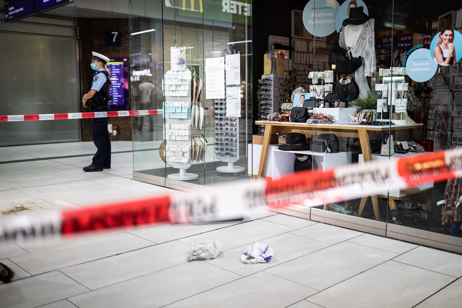 Einsatzkräfte der Polizei stehen im Hauptbahnhof vor einem Ladenlokal mit eingeschlagener Scheibe und Brandspuren auf dem Boden.