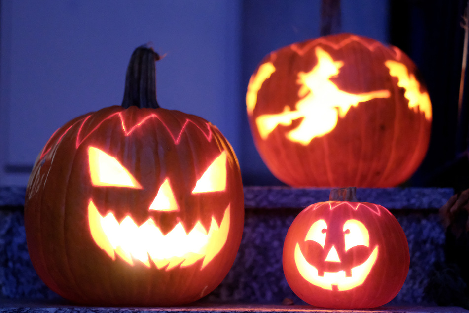 Geschnitzte Halloween-Kürbisse mit Geister-Motiven stehen von innen beleuchtet vor einem Haus.