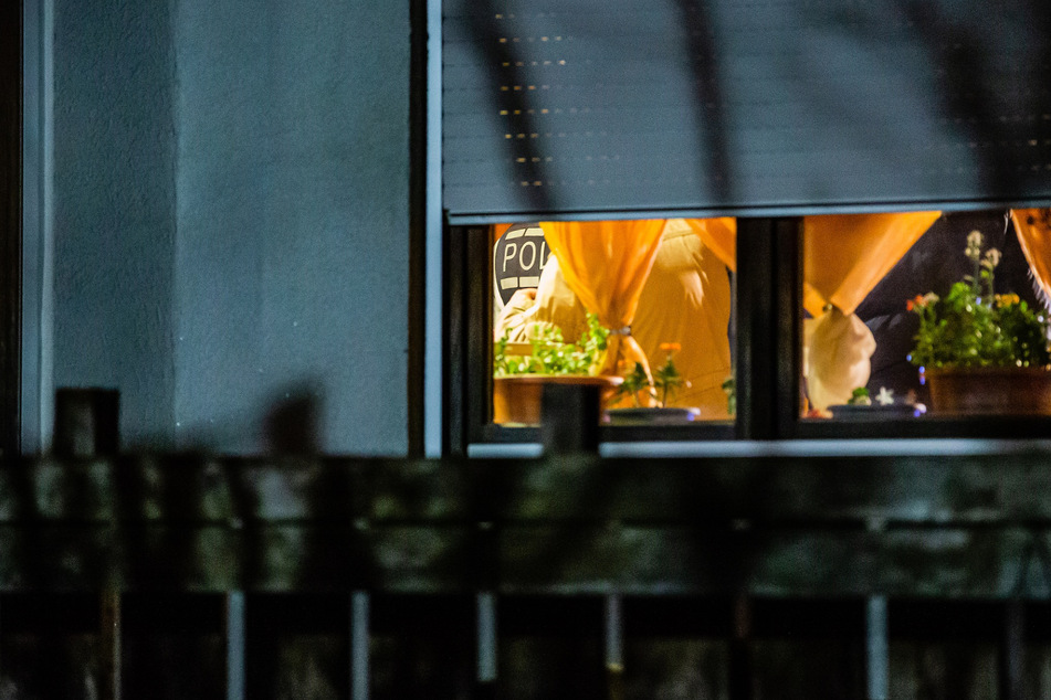 Durchs Fenster kann man einen Polizeibeamten erblicken, der sich in der gestürmten Wohnung aufhält.