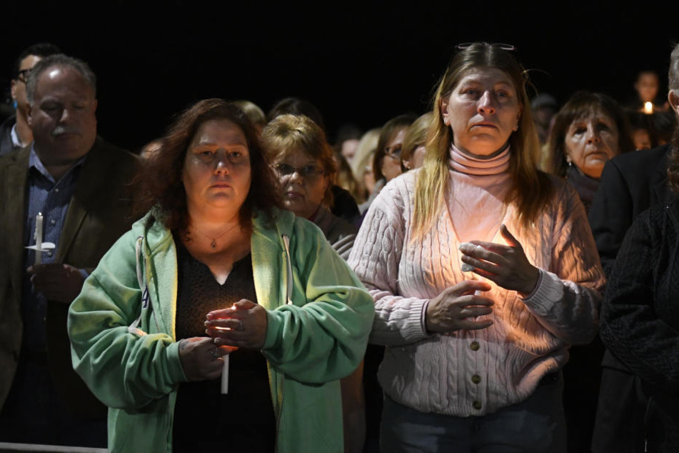 Maria Busch (l) und Tammy Smith nehmen mit anderen Angehörigen an einer Gedenkveranstaltung teil und halten Kerzen.