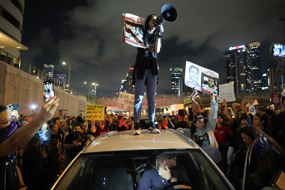 Einav holds a sign identifying her son Matan Zangauker, one of the hostages taken captive by Palestinian militants in the Gaza Strip during the October 7 attacks, as she stands on the roof of a car during a demonstration by hostages' relatives and supporters in the Israeli coastal city of Tel Aviv on May 6, 2024.