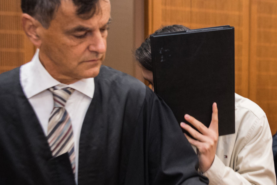 Der 27-jährige Angeklagte hält sich eine Mappe vor das Gesicht.