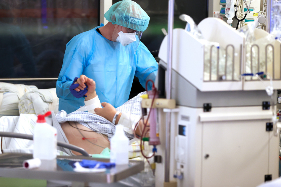 Ein Facharzt versorgt einen Covid-19-Patienten auf der Intensivstation der Leipziger Uniklinik und hält dessen Hand.