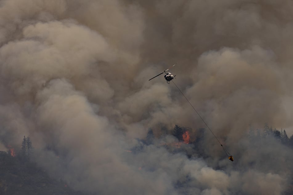 A firefighting helicopter flies near smoke and flames at the McKinney fire.