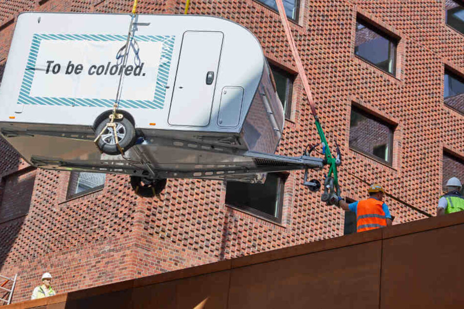 Arbeiter haben mit einem Kran einen Wohnwagen in der Hafencity in die Luft.