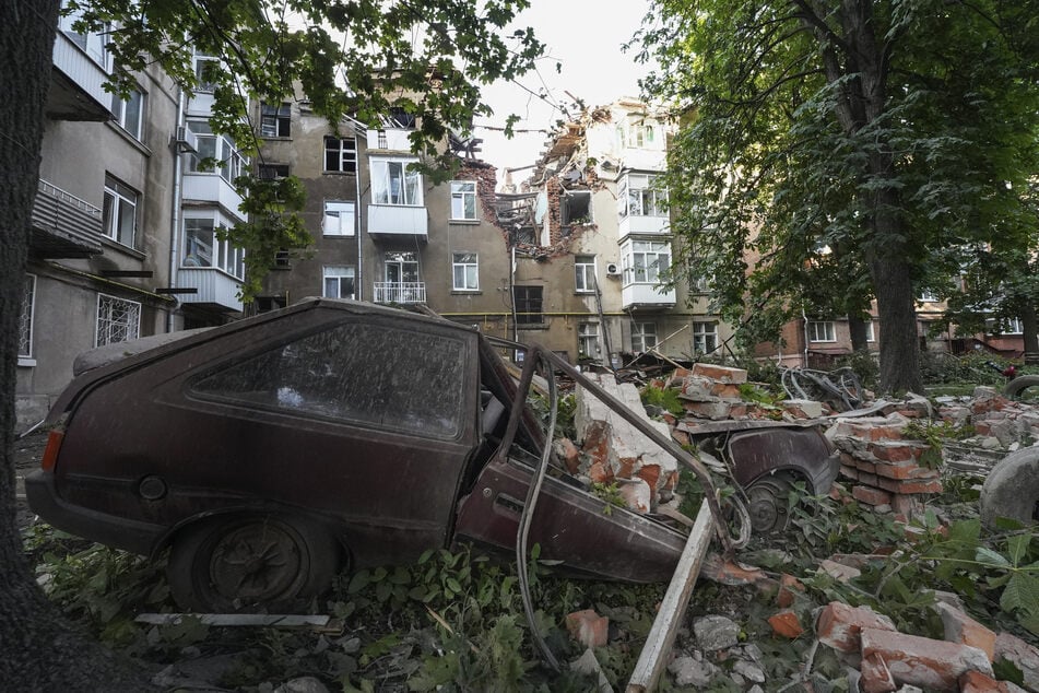 Ein Autowrack ist nach einem Angriff vor einem beschädigten Wohnhaus in Sumy zu sehen.