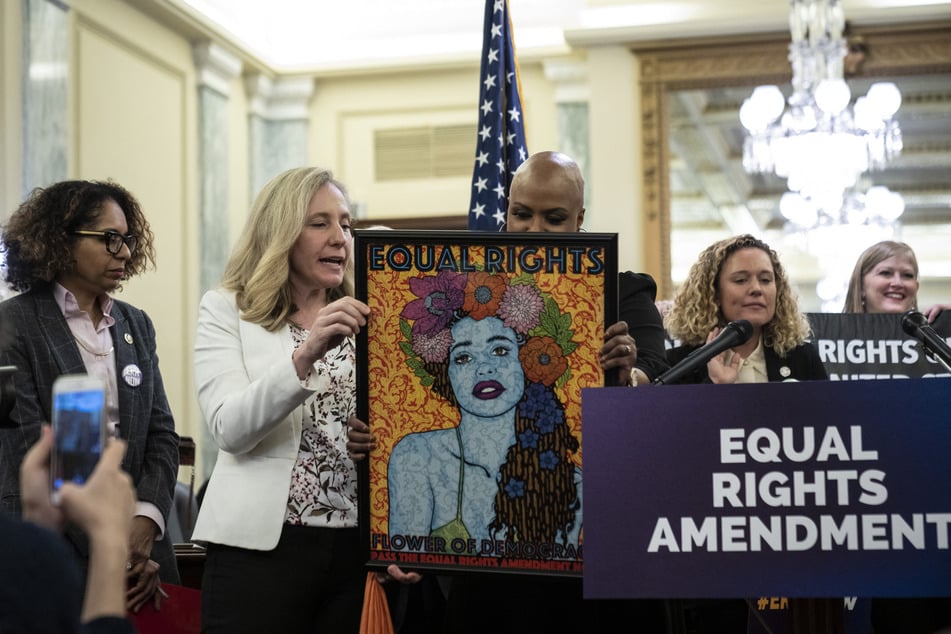 Rep. Abigail Spanberger (center l) shows a piece of art to Rep. Ayanna Pressley (center r) during a news conference to announce a joint ERA resolution on January 31 in Washington DC.