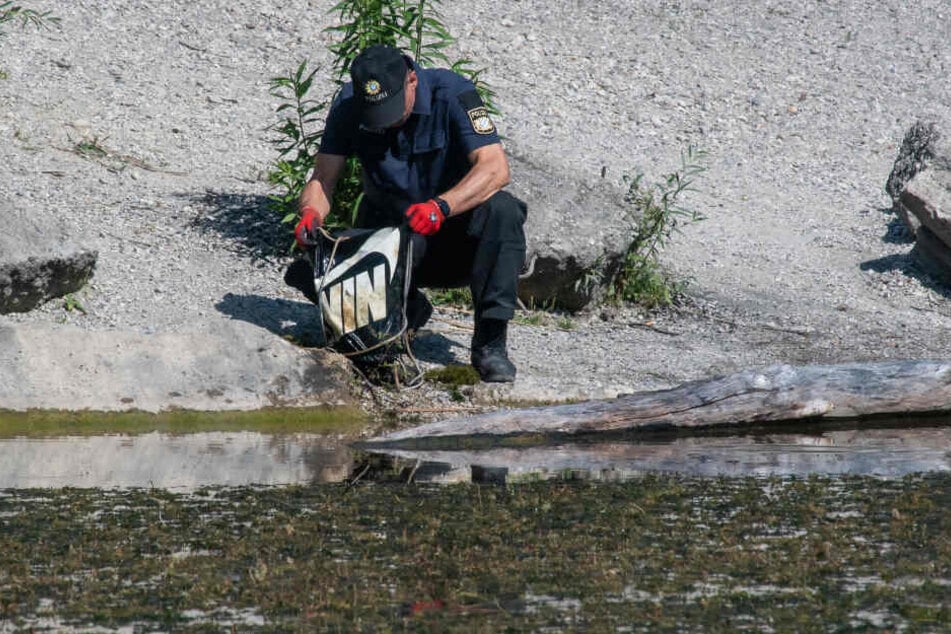 Ein Polizist durchsucht einen Turnbeutel, den Taucher im Baggersee im alten Kieswerk bei München gefunden haben.