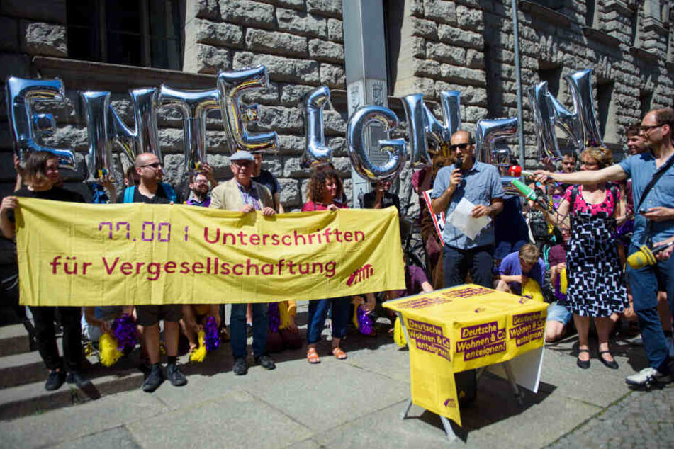 Rouzbeh Taheri, Sprecher der Initiative Deutsche Wohnen & Co enteignen, steht vor einem Transparent "77.001 Unterschriften für Vergesellschaftung".
