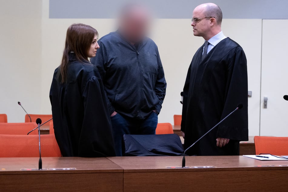 Der wegen fahrlässiger Tötung und fahrlässiger Körperverletzung angeklagte Mann (M.) steht vor Prozessbeginn mit seinen Anwälten Stephan Beukelmann (r.) und Mariana Sacher im Gerichtssaal.