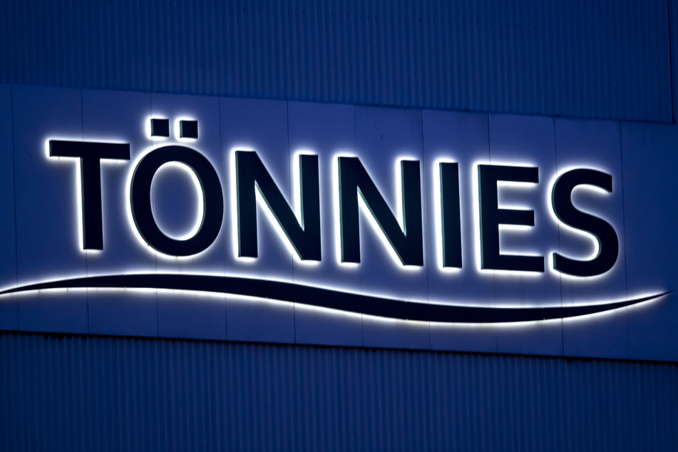 Das Logo und der Schriftzug der Firma Tönnies leuchten am frühen Morgen auf einem Schild an einem Gebäude des Fleischwerks Tönnies.