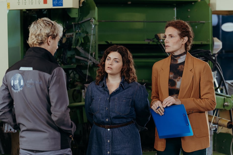 Lilli Gruber (Ronja Forcher, M.) und Caro Pflüger (Barbara Lanz, r.) warten gespannt auf den Bericht von Xaver Hofinger (David Ali Rashed, l.). Sind die gekauften landwirtschaftlichen Fahrzeuge in einwandfreiem Zustand?