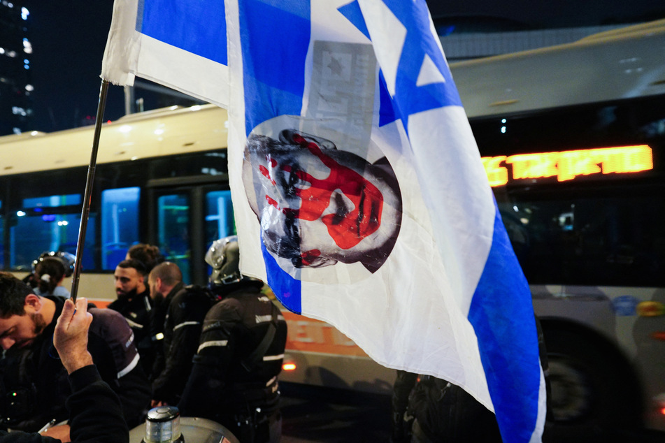 A person holds an Israeli flag with an image depicting Israeli Prime Minister Benjamin Netanyahu as people protest against his government in Tel Aviv.