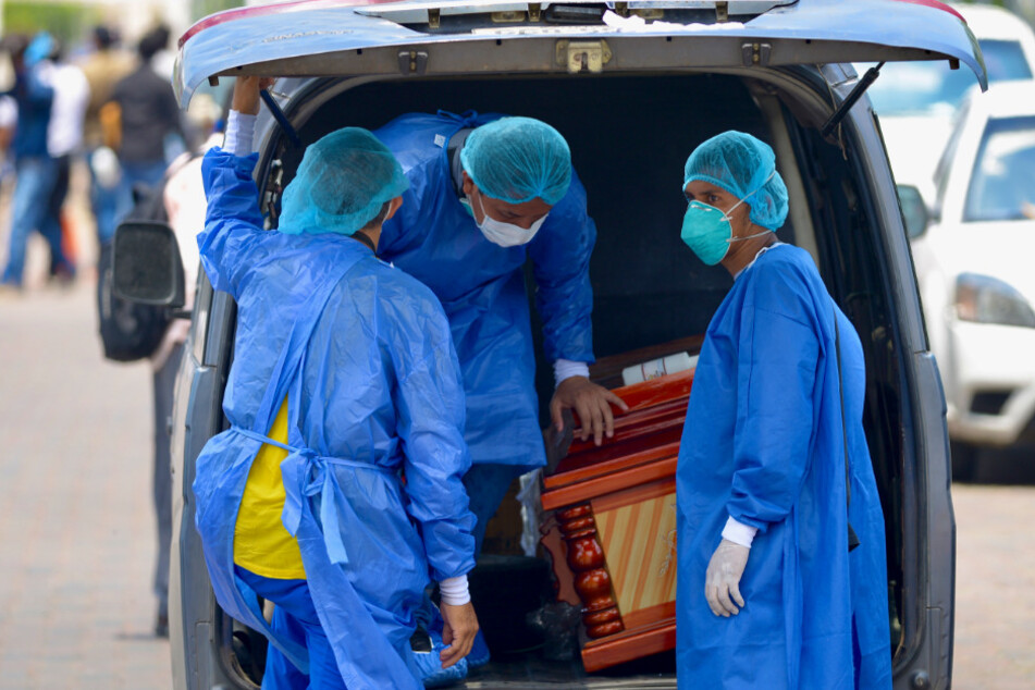 Männer mit Schutzanzügen laden einen Sarg in einen Wagen vor dem Krankenhaus General del Guasmo.