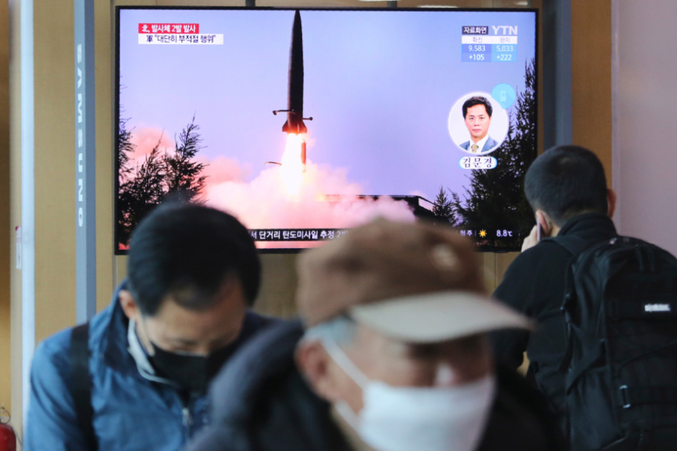 Südkorea, Seoul: Menschen gehen an einem Fernsehbildschirm vorbei, während eine Nachrichtensendung den Start einer Rakete in Nordkorea zeigt.