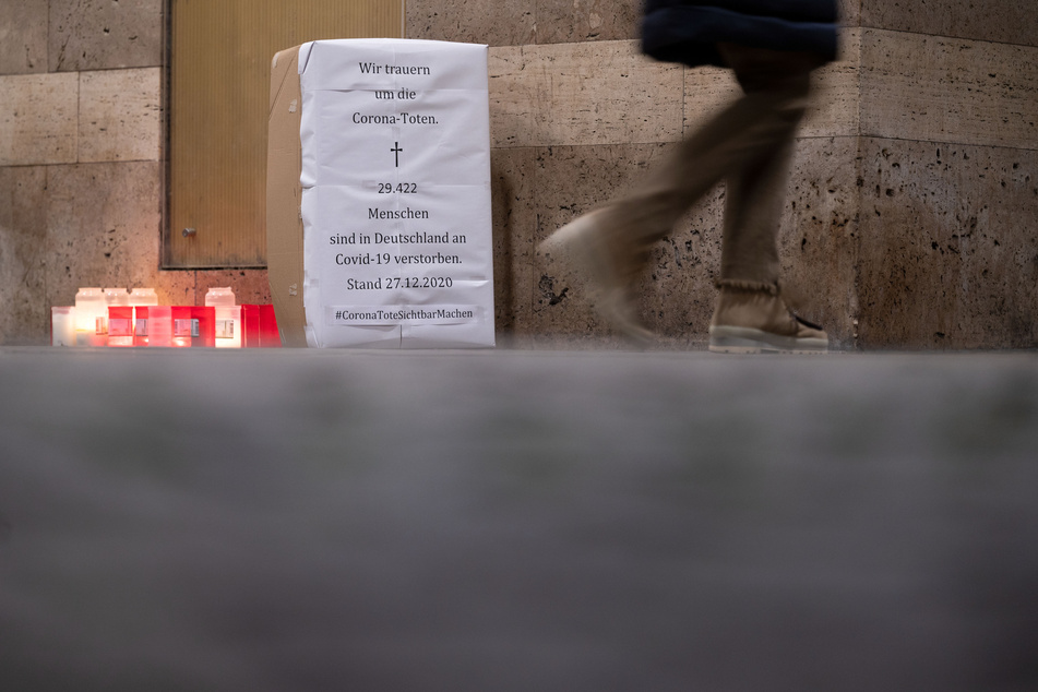 Baden-Württemberg, Stuttgart: Eine Frau geht an einem Karton vorbei, der mit einem Plakat beklebt ist, auf dem steht: "Wir trauern um die Corona-Toten. 29.422 Menschen sind in Deutschland an Covid-19 verstorben. Stand 27.12.2020".