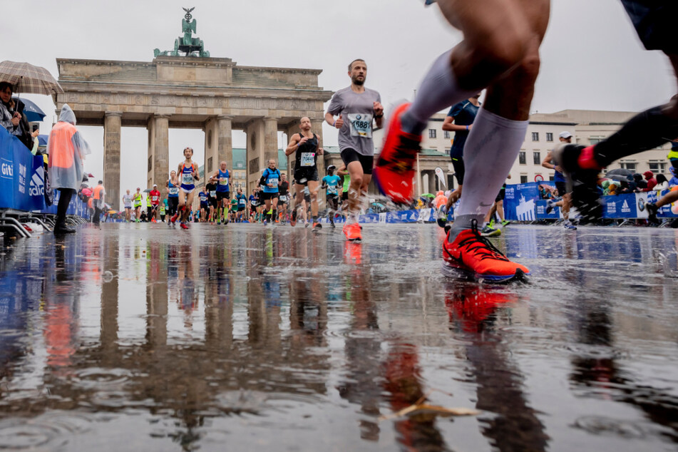 Teilnehmer des 46. Berlin-Marathons laufen bei Regen kurz vor der Ziellinie vor dem Brandenburger Tor.