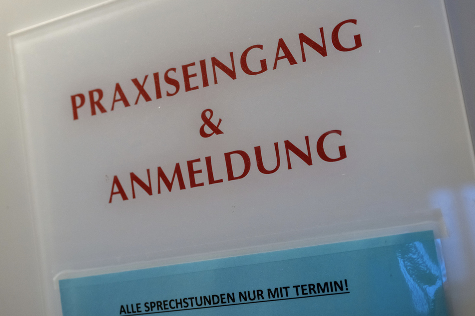 Ein Schild an einer Hauswand weist auf den Eingang einer Arztpraxis hin. Die Zahl der Ärztinnen und Ärzte in Bayern hat vergangenes Jahr einen neuen Rekordwert erreicht.