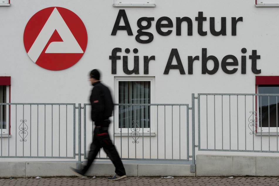 Ein Mann geht an dem Logo der Agentur für Arbeit vorbei.