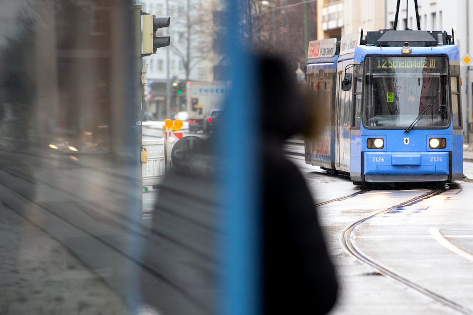 Eine Frau wartet an einer Haltestelle auf eine Straßenbahn. In Bayern gilt vom kommenden Montag an eine Pflicht zum Tragen von FFP2-Masken im öffentlichen Nahverkehr und im Einzelhandel.