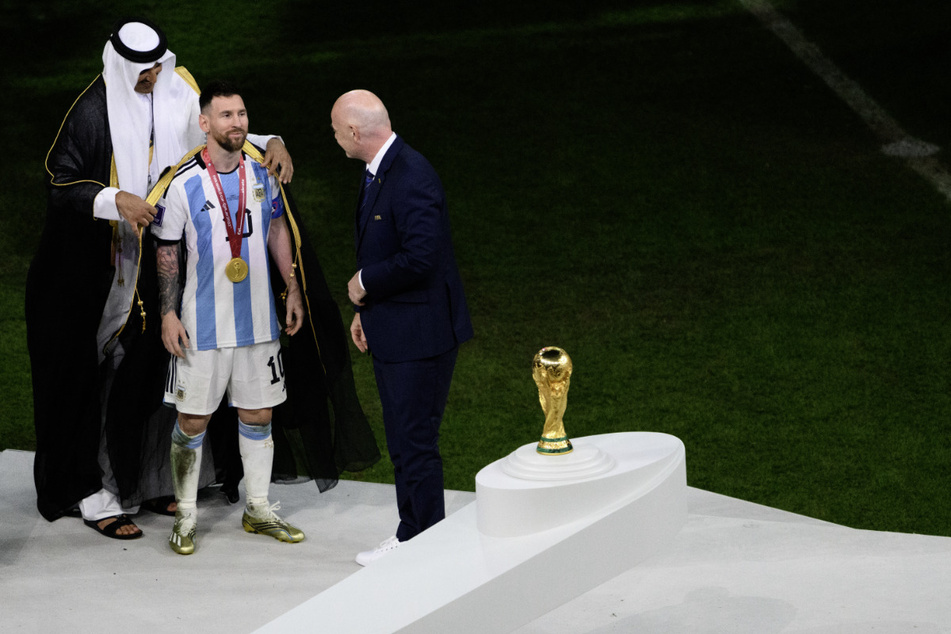Der Emir von Katar, Scheich Tamim bin Hamad Al Thani (42, l), legte Lionel Messi (35) vor Übergabe des WM-Pokals vor Fifa-Präsident Gianni Infantino (52) ein Bischt an.