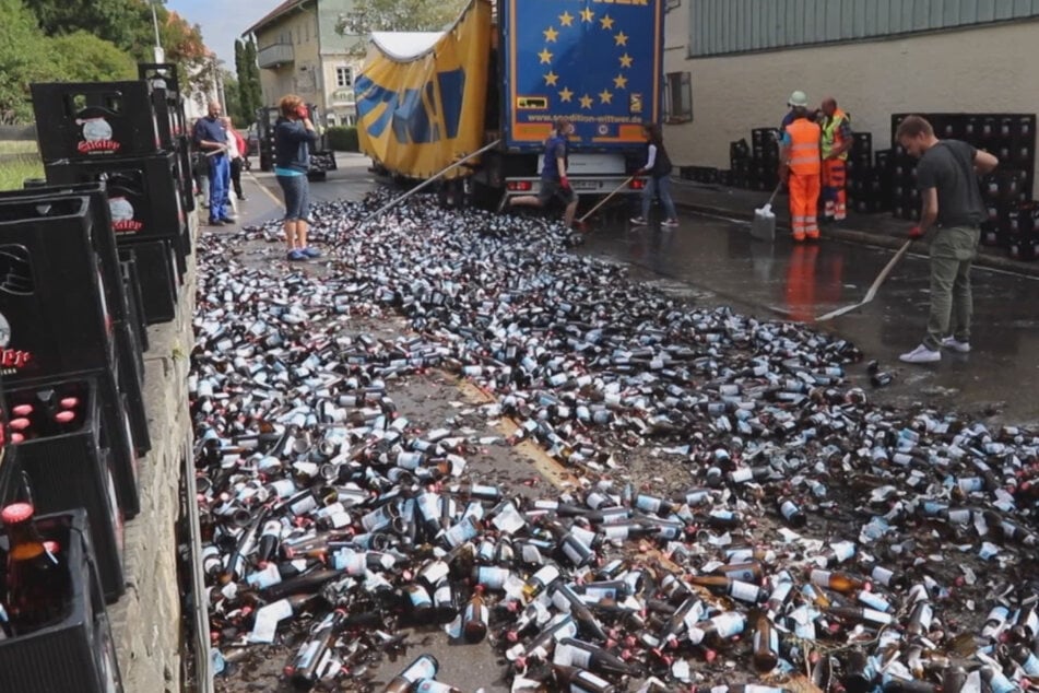 Einsatzkräfte von der Feuerwehr sowie Helfer räumen zahlreiche zerbrochene Bierflaschen auf.